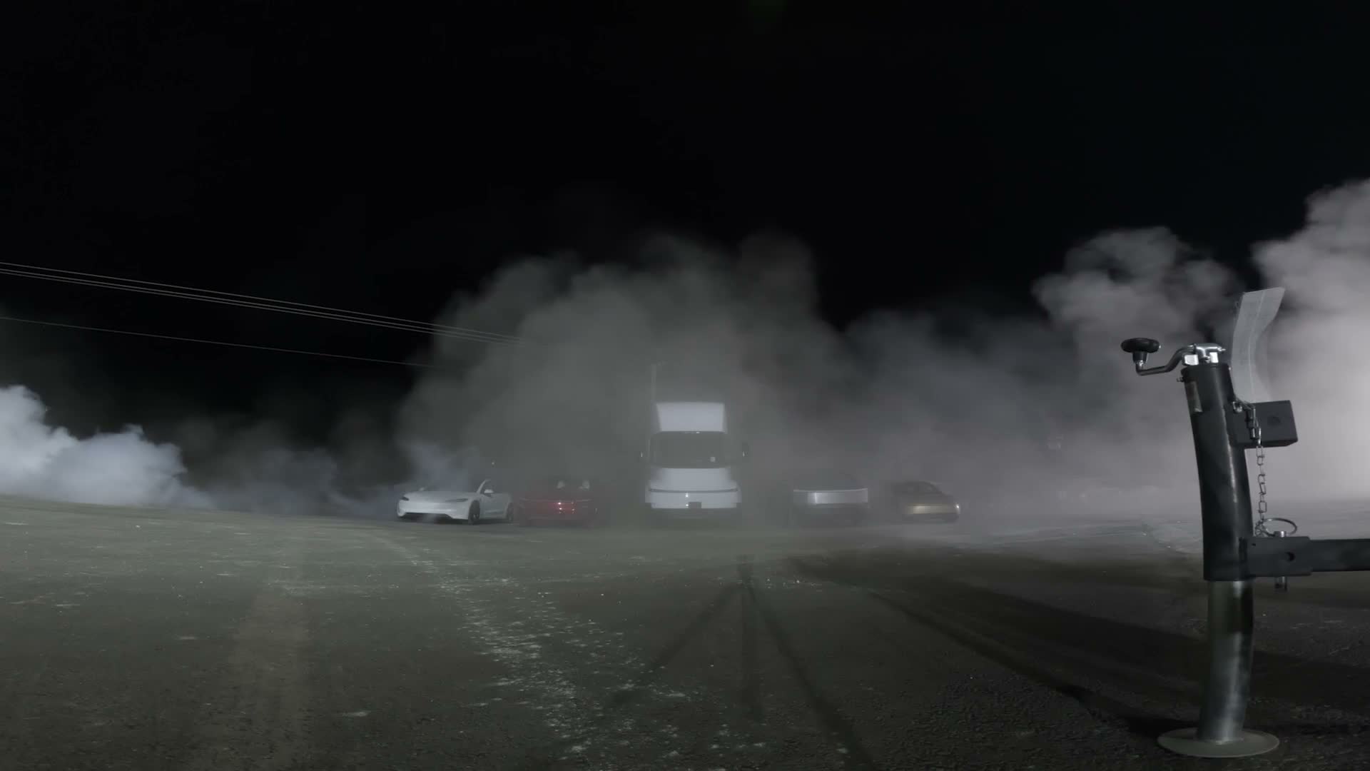 The Tesla lineup in vapor at night after the Roadster's jump — a white Tesla, the red Roadster, a Semi and a Cybertruck