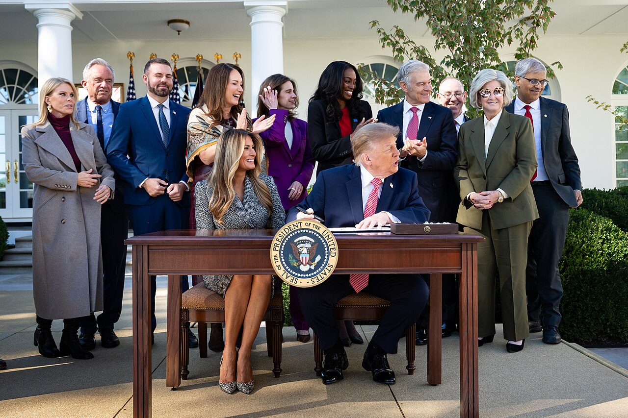 Melania Trump seated beside President Trump at a White House signing.